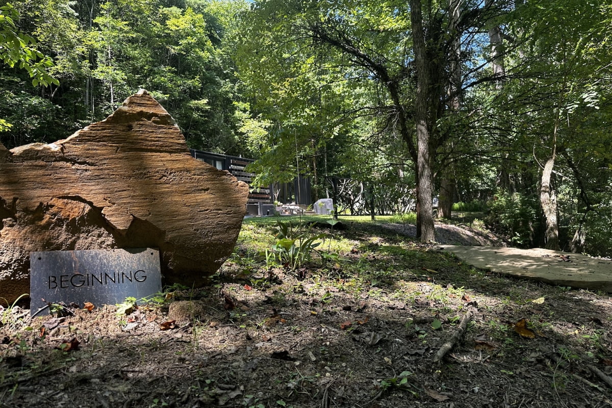 A sign reading "begining" placed in front of a large, weathered rock formation amidst a verdant, forested park area, highlighting the benefits of nature.