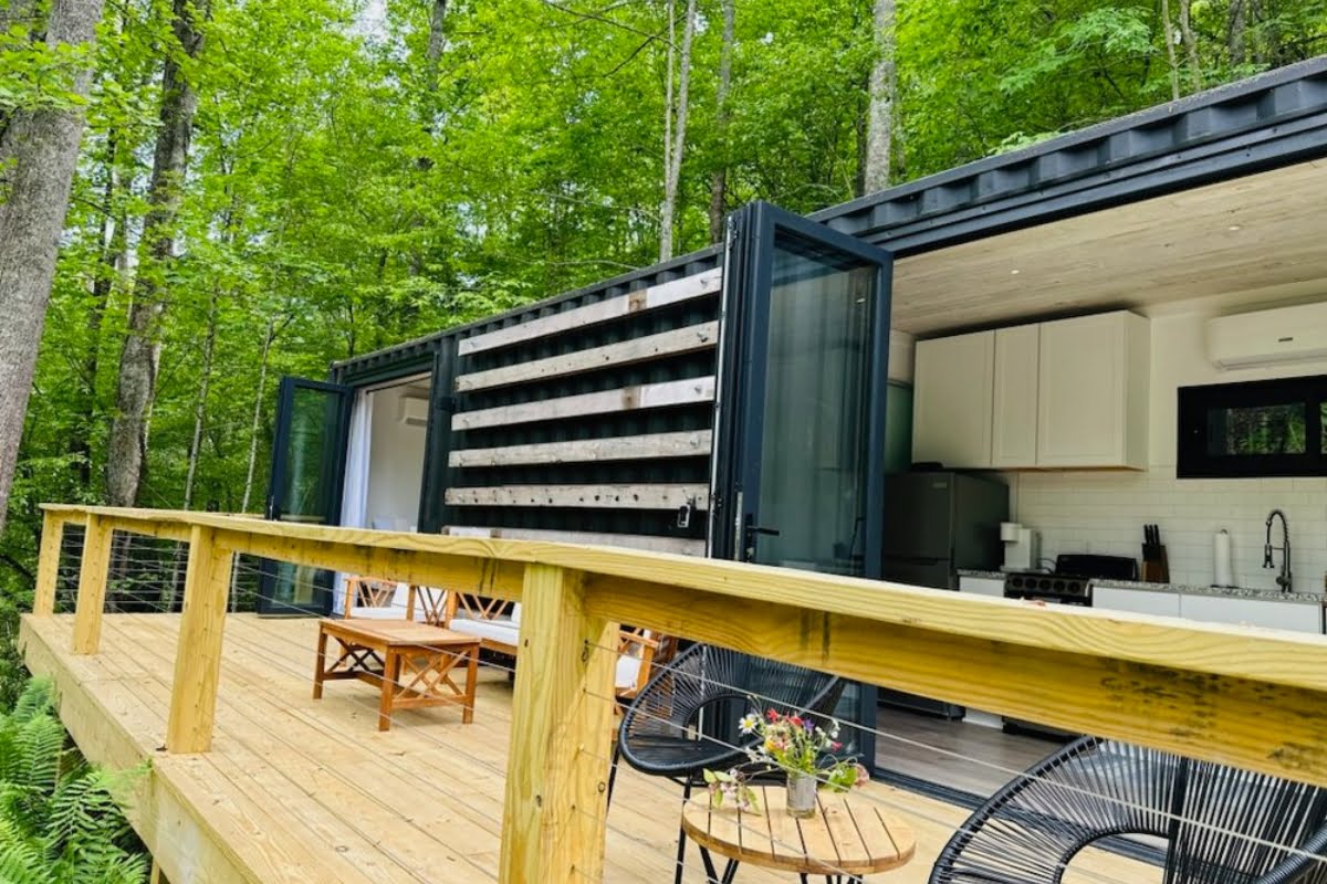 Modern shipping container home with an outdoor wooden deck in a forest setting, offering a perfect Nature Rx escape.