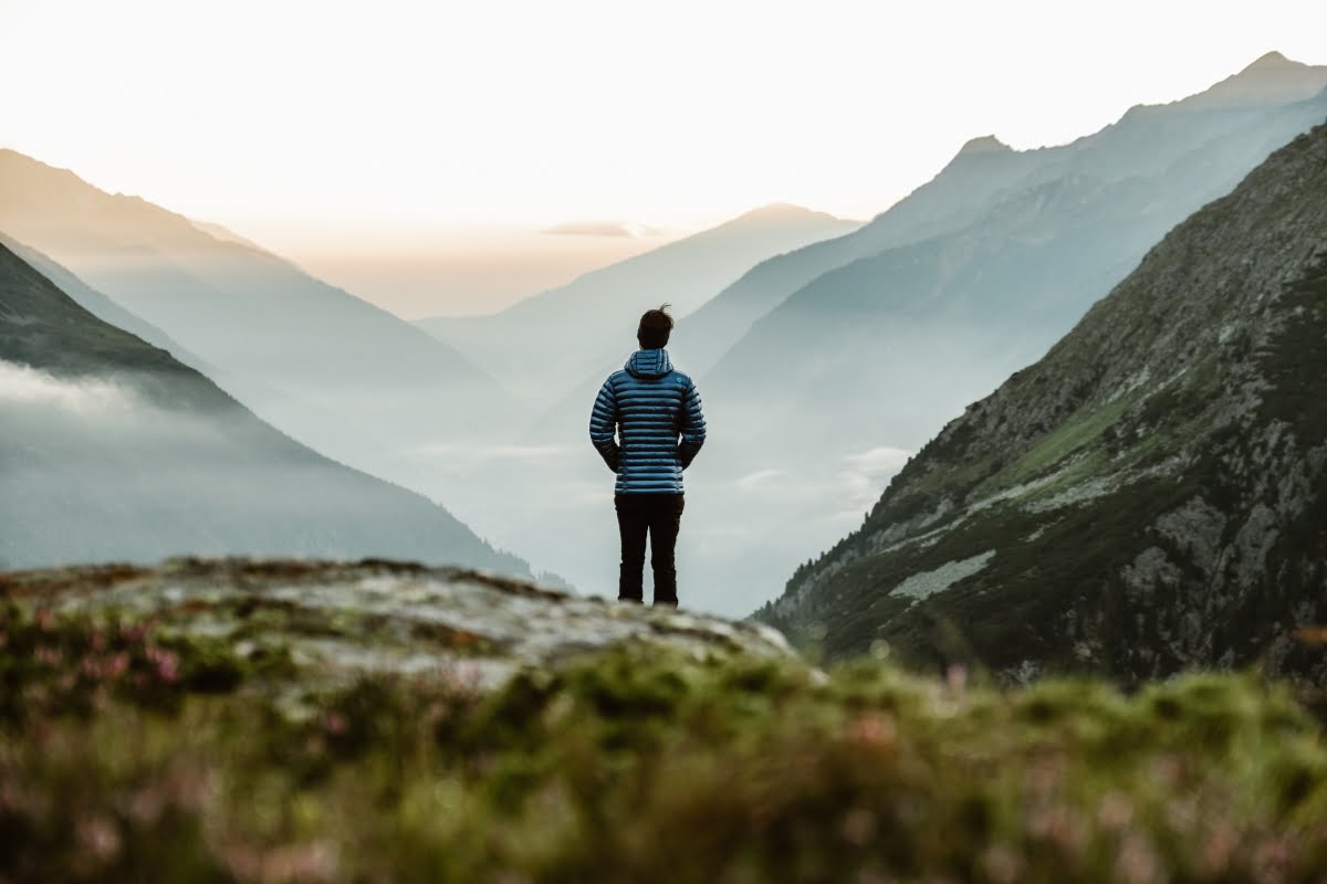 A person standing on a mountain ledge overlooking a misty valley at Basecamp Smokey Mountains retreat enjoying the benefits of nature.