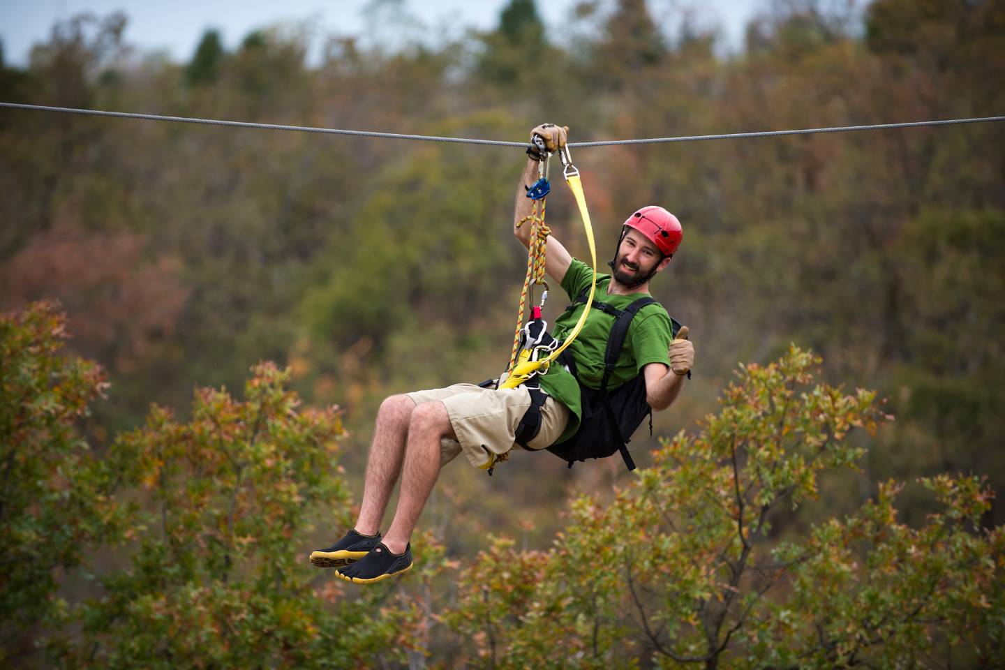 A person wearing a helmet and safety gear is experiencing the thrill of Basecamp's zipline tour through a wooded area.