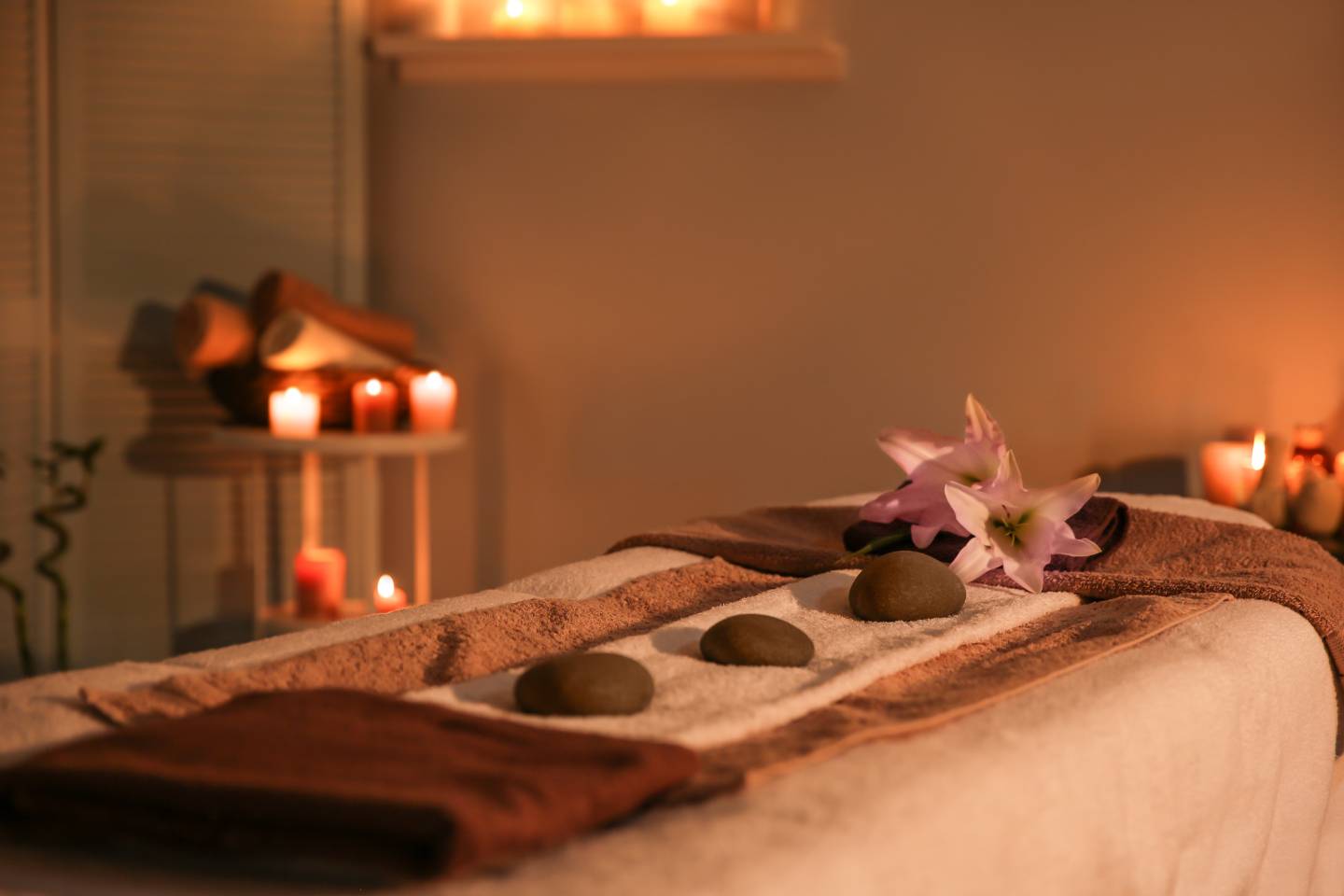 A serene spa experience with a massage table covered in a towel, adorned with stones and orchids, and ambient candles in the background.