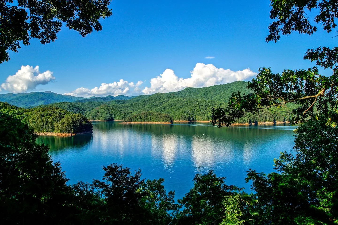 A serene lake surrounded by lush green mountains under a clear blue sky, with reflections visible in the calm water, is one of the local attractions as well as whitewater kayaking.