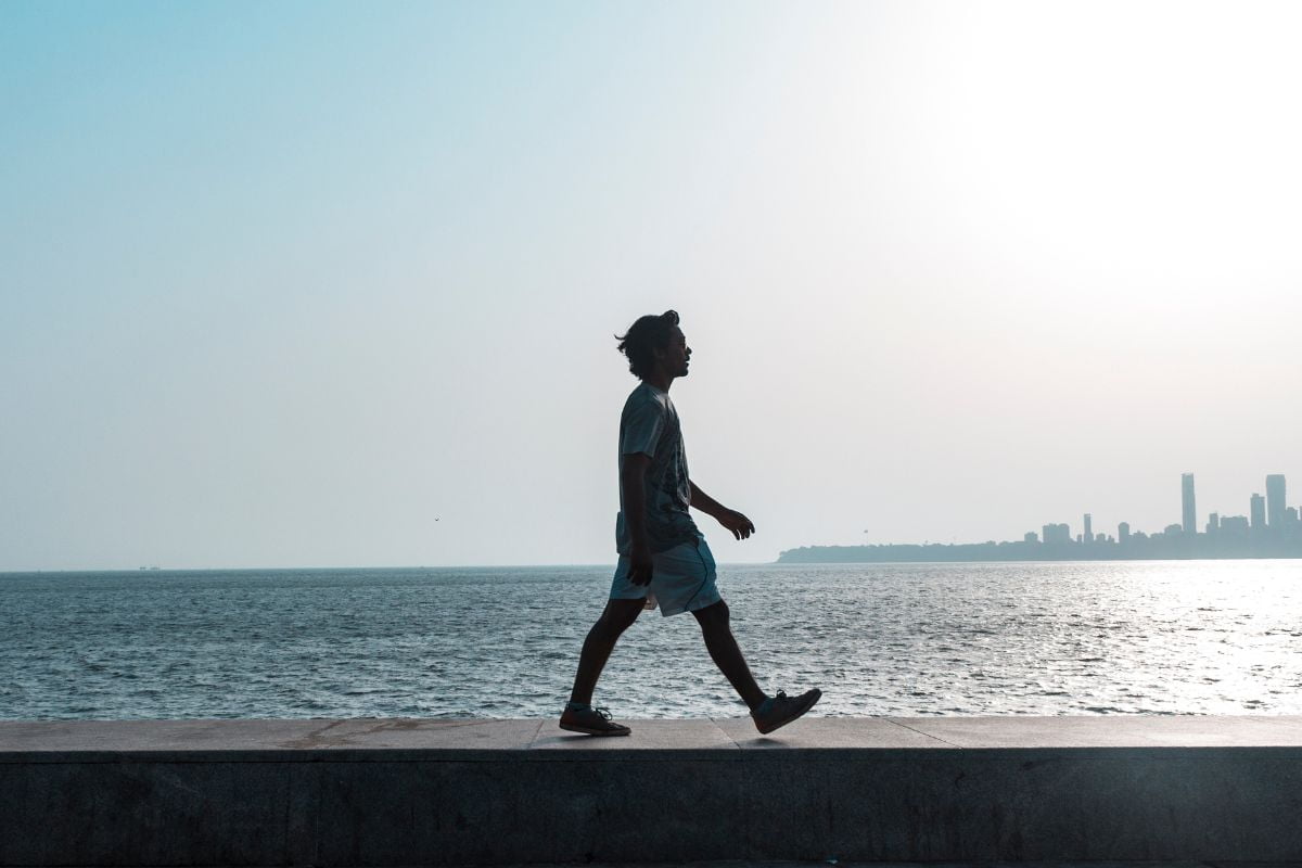 A person engaging in the art of mindful walking along a seaside promenade at sunset, with a city skyline in the background.