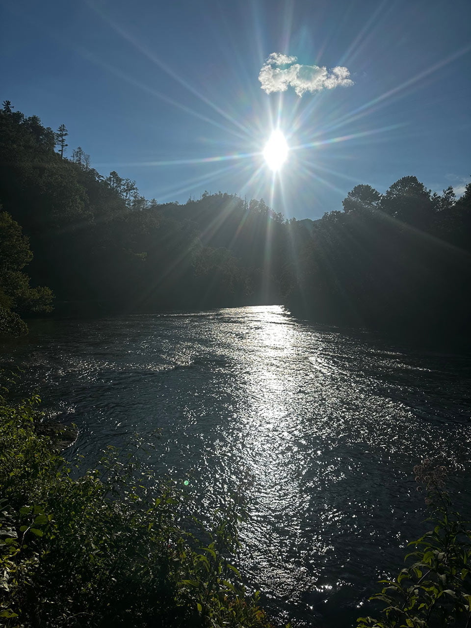 Sunlight shining down on a river in the Smoky Mountains, creating bright reflections on the water with trees on the surrounding hillsides.