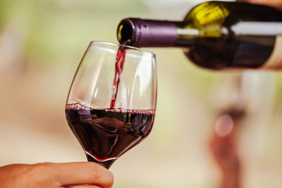 A person pours red wine from a bottle into a glass, which is held by another person, creating the perfect moment for shared culinary experiences.