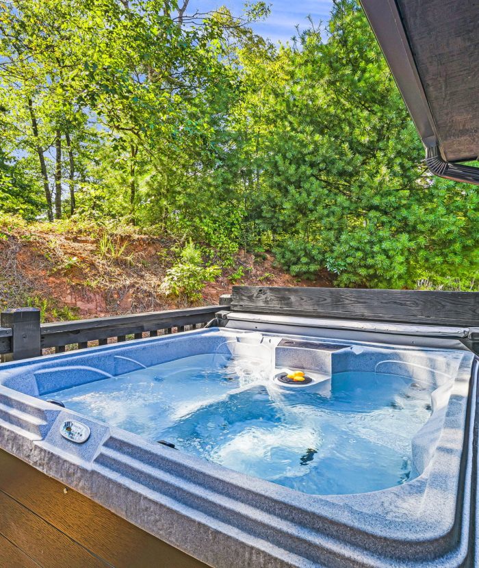 Outdoor hot tub on a deck, surrounded by lush greenery and trees.