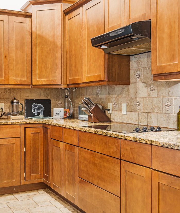 A kitchen with wooden cabinets, granite countertops, and black appliances, including a refrigerator, stove, and oven. Small kitchen appliances and utensils are placed on the countertops.