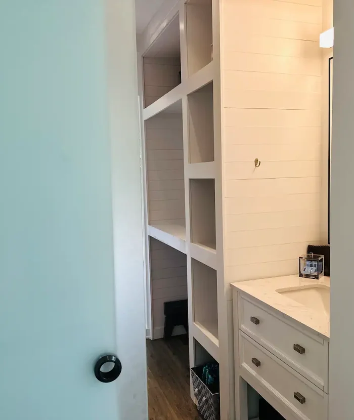 Our Elevation Eco-Villa has a small, well-lit bathroom with white cabinetry, built-in shelves, and a beige countertop. a partial view of a blue door is visible on the left.