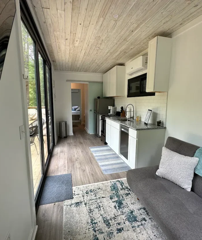 Interior of our Elevation Eco-Villa showing a kitchen area with appliances and a living space with a gray sofa, leading through to a bedroom.